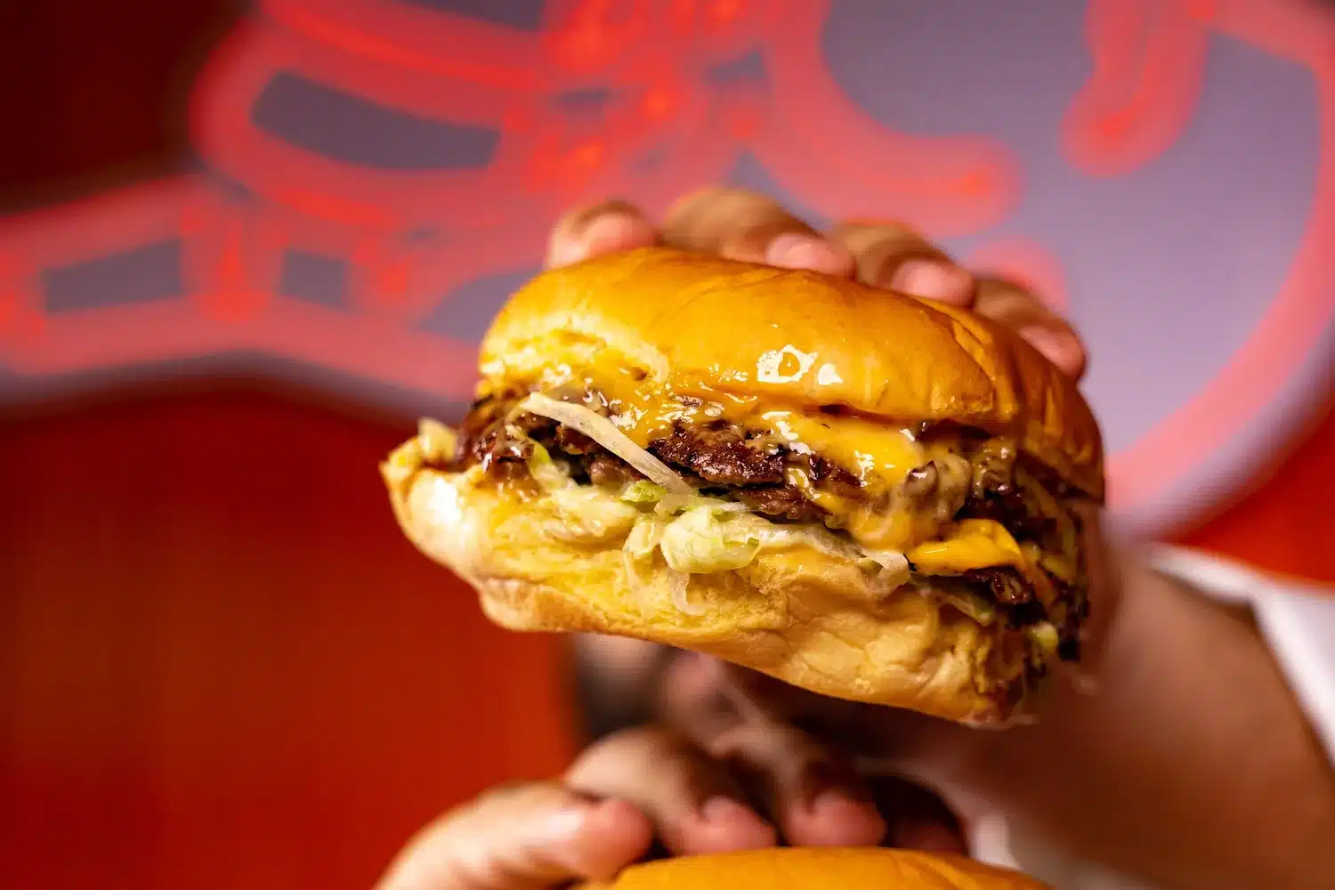 Deux smash burgers au fromage fondu tenus à pleines mains, pain brioché doré