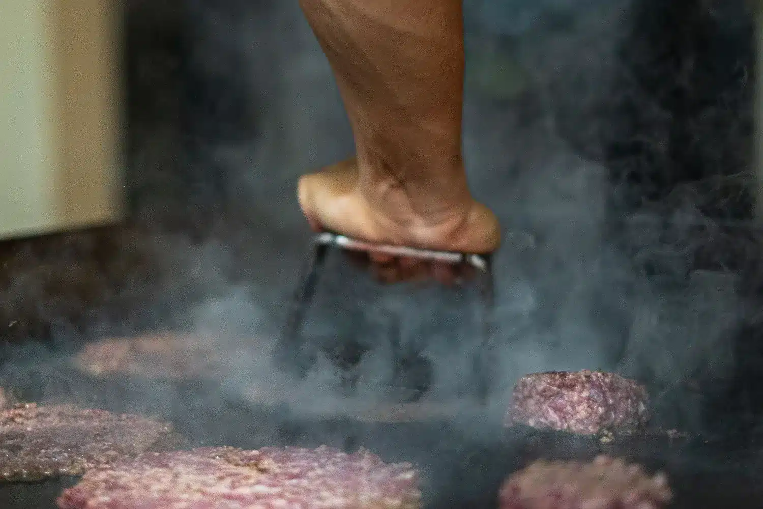 Main pressant des steaks hachés à la spatule sur une plancha fumante